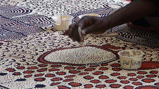 Traditionelle Aborigine-Punktmalerei mit erdigen Farbtönen, kreisförmigen Mustern und symbolischen Darstellungen von Traumzeitgeschichten.